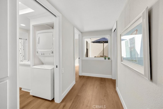 corridor with a textured ceiling, light wood-style floors, stacked washer / drying machine, and baseboards