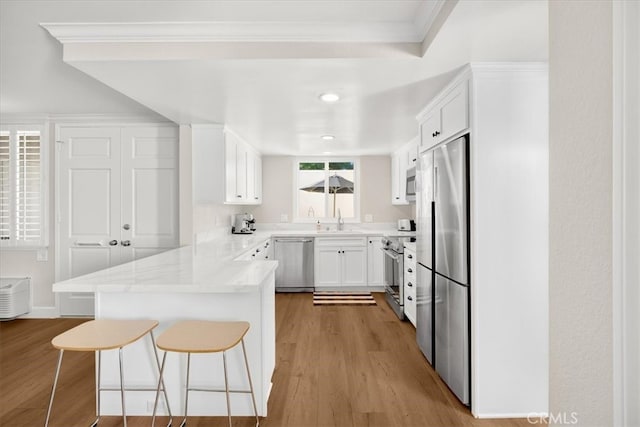 kitchen with a breakfast bar, light wood-type flooring, appliances with stainless steel finishes, a peninsula, and white cabinetry