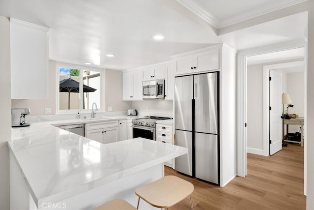 kitchen featuring light wood-type flooring, appliances with stainless steel finishes, a peninsula, white cabinetry, and a sink