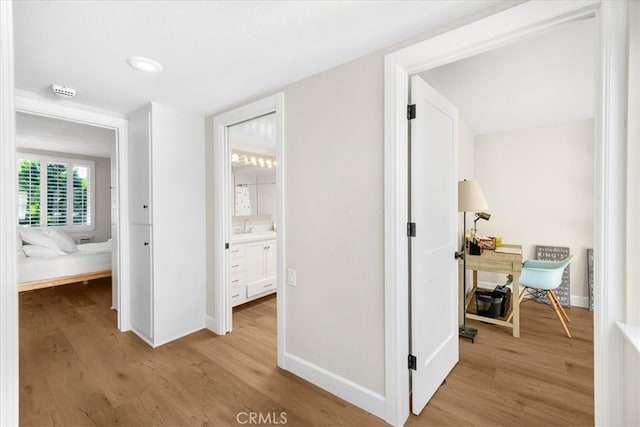 hallway featuring baseboards, light wood finished floors, and a sink