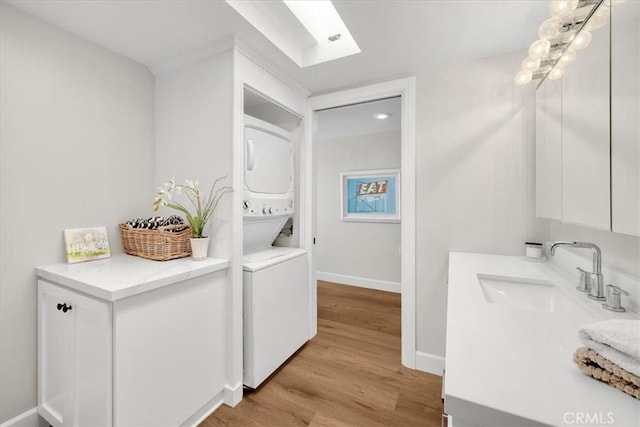 clothes washing area featuring stacked washing maching and dryer, laundry area, a skylight, light wood-style flooring, and a sink