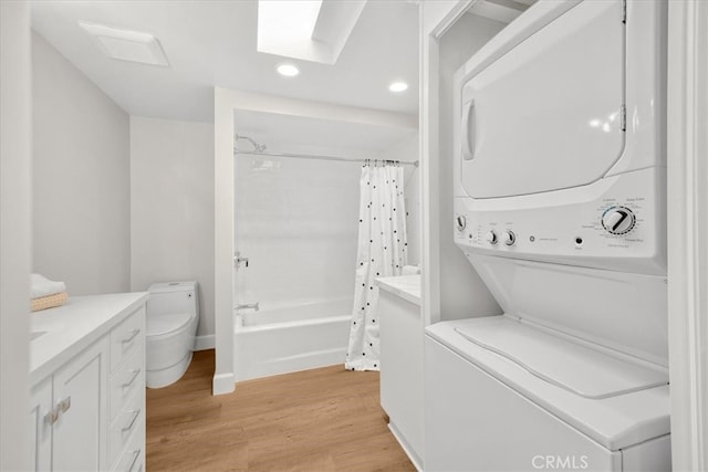 laundry room with light wood-style flooring, recessed lighting, a skylight, stacked washer / dryer, and laundry area