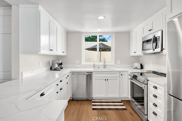 kitchen with light wood-type flooring, a sink, white cabinetry, stainless steel appliances, and light stone countertops