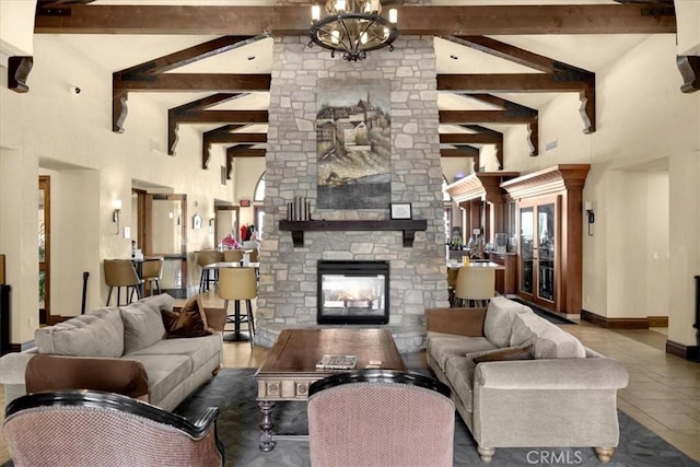 living area with baseboards, high vaulted ceiling, an inviting chandelier, beam ceiling, and a stone fireplace