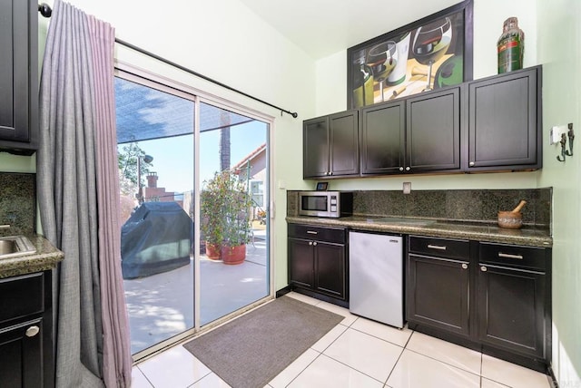 kitchen featuring fridge, stainless steel microwave, light tile patterned flooring, and dark countertops