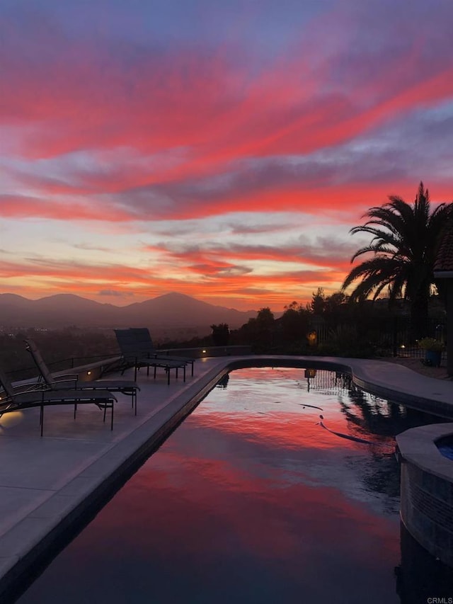 pool at dusk featuring a pool with connected hot tub, a patio area, a mountain view, and central AC