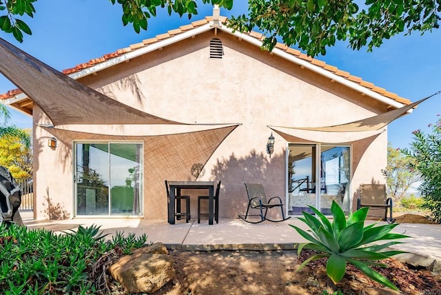 rear view of property with a tiled roof, a patio area, and stucco siding