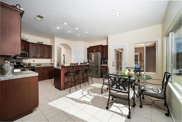 1185 Cedar Summit Dr, Ramona, CA 92065 - kitchen featuring stainless steel appliances, a kitchen island, a kitchen breakfast bar, arched walkways, and light tile patterned floors