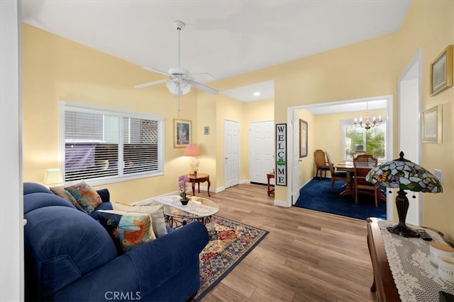 living room with light wood finished floors, ceiling fan with notable chandelier, and baseboards