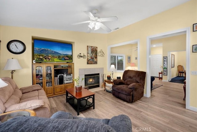 living room featuring light wood-type flooring, visible vents, baseboards, ceiling fan, and a tile fireplace