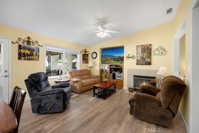 living area with visible vents, light wood finished floors, lofted ceiling, ceiling fan, and a tile fireplace