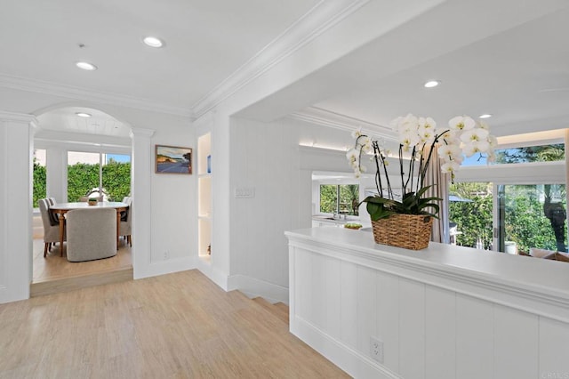 corridor featuring arched walkways, plenty of natural light, crown molding, and light wood-style floors