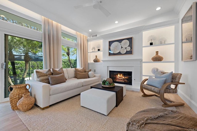 living room with a glass covered fireplace, built in shelves, wood finished floors, and visible vents