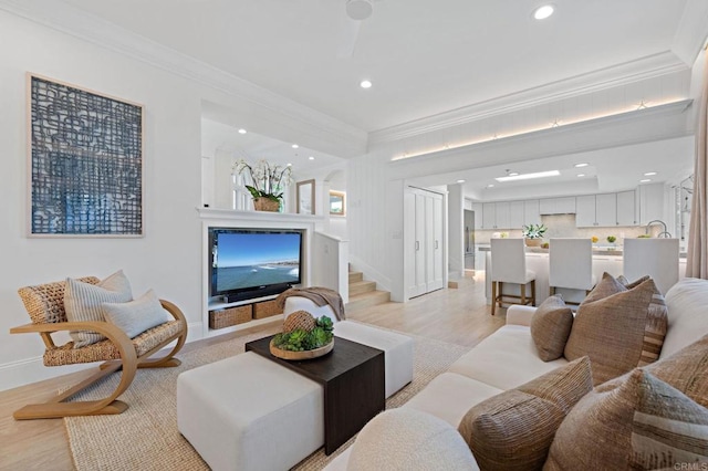 living room featuring crown molding, baseboards, light wood-type flooring, stairs, and recessed lighting