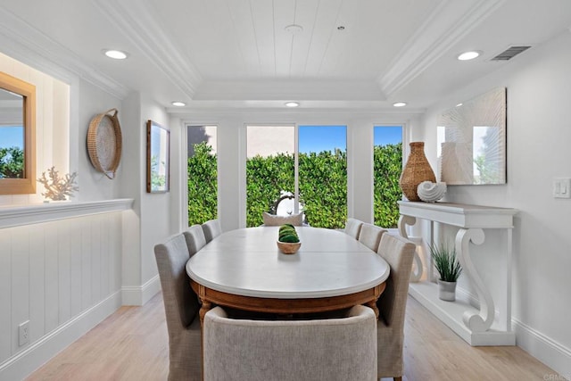 dining area with visible vents, a raised ceiling, ornamental molding, and light wood finished floors