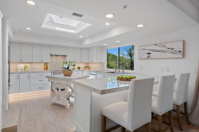 kitchen with visible vents, a kitchen breakfast bar, a skylight, white cabinets, and a raised ceiling