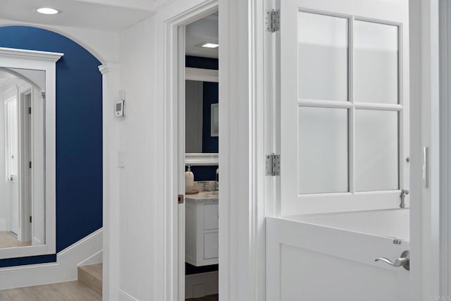 hallway featuring arched walkways, recessed lighting, baseboards, and wood finished floors