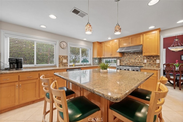 kitchen featuring visible vents, a kitchen island, under cabinet range hood, a breakfast bar, and decorative backsplash