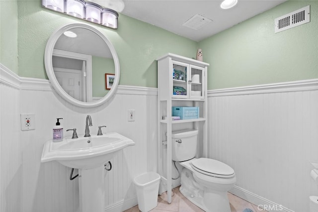 half bath with visible vents, toilet, and a wainscoted wall