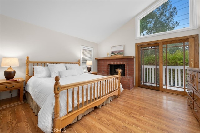 bedroom with high vaulted ceiling, a brick fireplace, wood finished floors, and access to outside