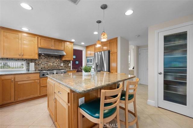 kitchen featuring under cabinet range hood, light stone counters, tasteful backsplash, a center island, and appliances with stainless steel finishes