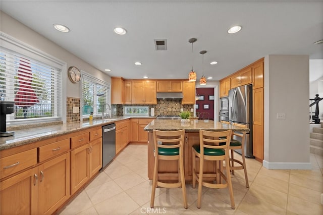 kitchen featuring a sink, tasteful backsplash, a center island, stainless steel appliances, and light stone countertops