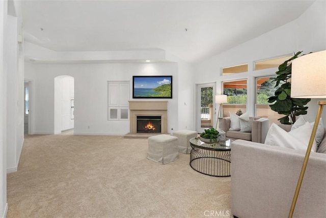 carpeted living area featuring vaulted ceiling, baseboards, arched walkways, and a lit fireplace