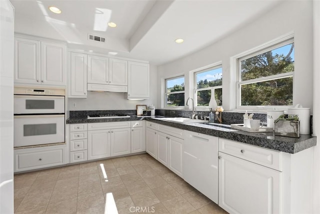 kitchen featuring visible vents, a sink, white cabinets, under cabinet range hood, and double oven