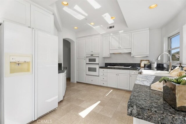 kitchen featuring visible vents, under cabinet range hood, white cabinets, white appliances, and a sink