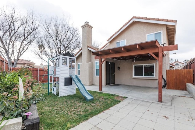 back of property with a fenced backyard, a chimney, stucco siding, a playground, and a patio area