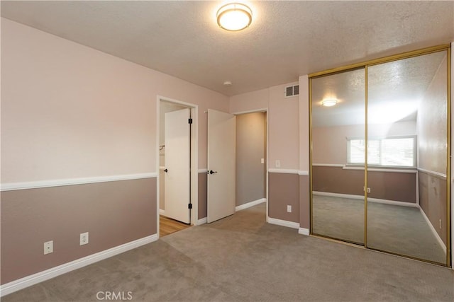 unfurnished bedroom featuring visible vents, carpet floors, a textured ceiling, and a closet