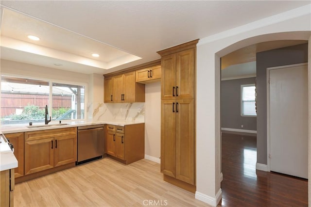 kitchen featuring light countertops, stainless steel dishwasher, light wood-style floors, arched walkways, and a sink