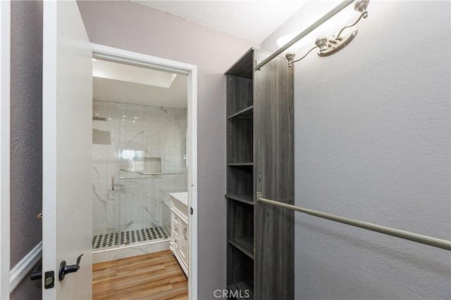 bathroom featuring a marble finish shower, wood finished floors, vanity, and a textured wall