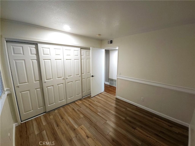 unfurnished bedroom featuring visible vents, a textured ceiling, wood finished floors, a closet, and baseboards