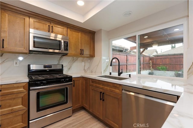 kitchen with a sink, brown cabinetry, tasteful backsplash, and stainless steel appliances