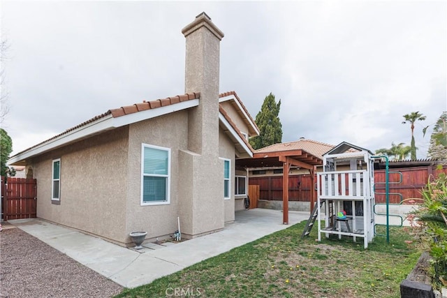 rear view of property featuring a fenced backyard, a chimney, stucco siding, a playground, and a patio area