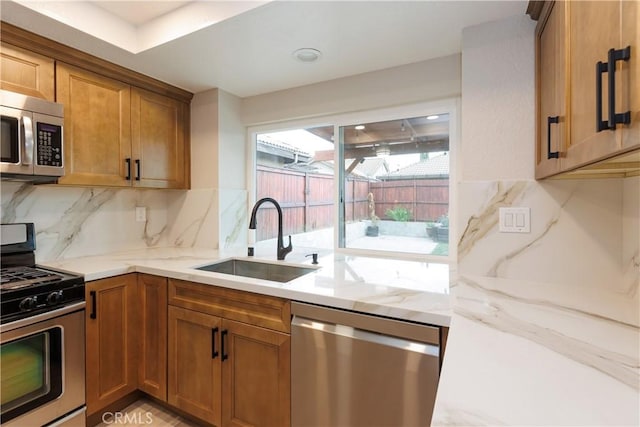 kitchen with a sink, light stone countertops, appliances with stainless steel finishes, and brown cabinetry