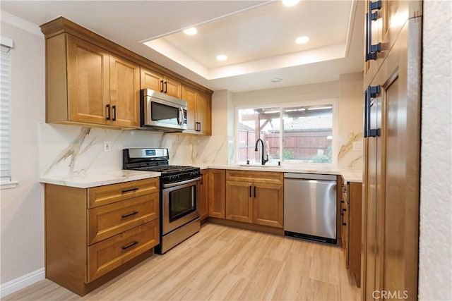 kitchen featuring a raised ceiling, brown cabinetry, appliances with stainless steel finishes, and a sink