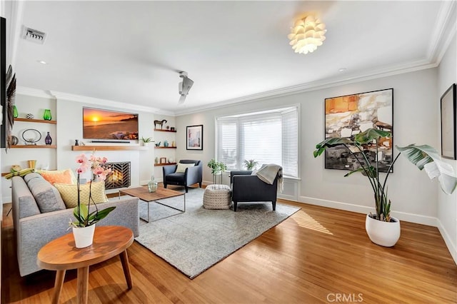 living area featuring visible vents, wood finished floors, a tiled fireplace, and ornamental molding