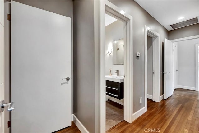 hallway featuring a sink, wood finished floors, visible vents, and baseboards