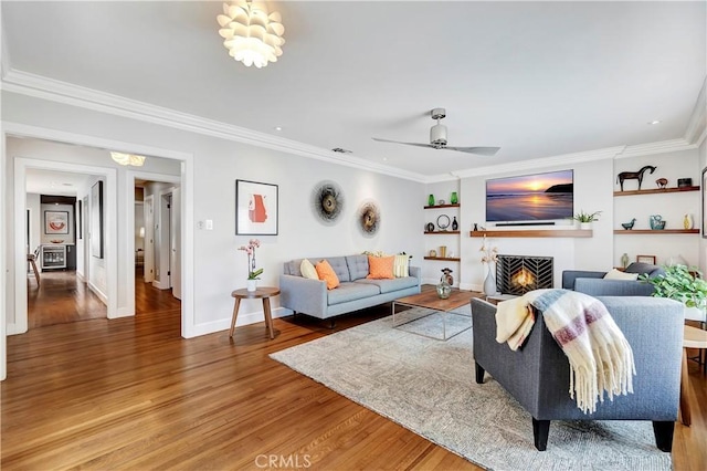 living area featuring a warm lit fireplace, light wood-style floors, crown molding, baseboards, and ceiling fan