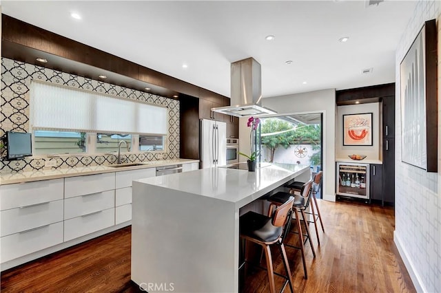 kitchen with modern cabinets, beverage cooler, island exhaust hood, appliances with stainless steel finishes, and light countertops