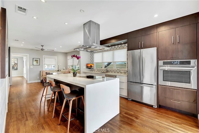 kitchen with visible vents, light wood-style flooring, a kitchen breakfast bar, stainless steel appliances, and island range hood