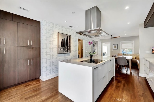 kitchen featuring island range hood, wood finished floors, black electric stovetop, modern cabinets, and a center island