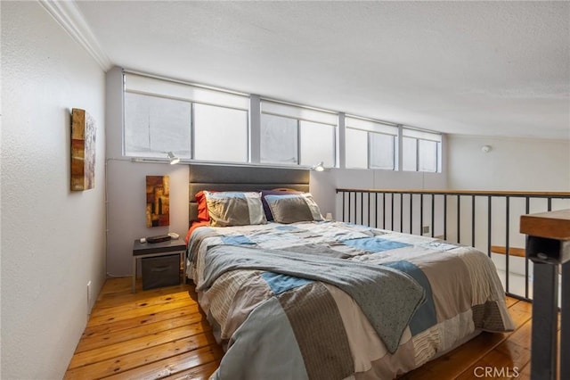 bedroom featuring crown molding, light wood-style flooring, a textured wall, and a textured ceiling