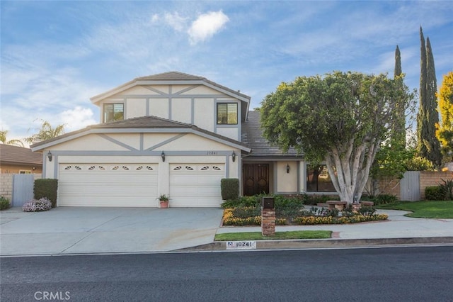 tudor house with stucco siding, a garage, concrete driveway, and fence