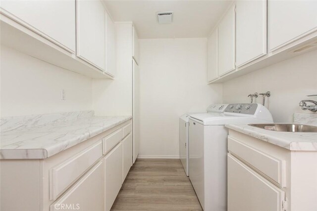 clothes washing area featuring visible vents, cabinet space, a sink, light wood-style floors, and washer and clothes dryer