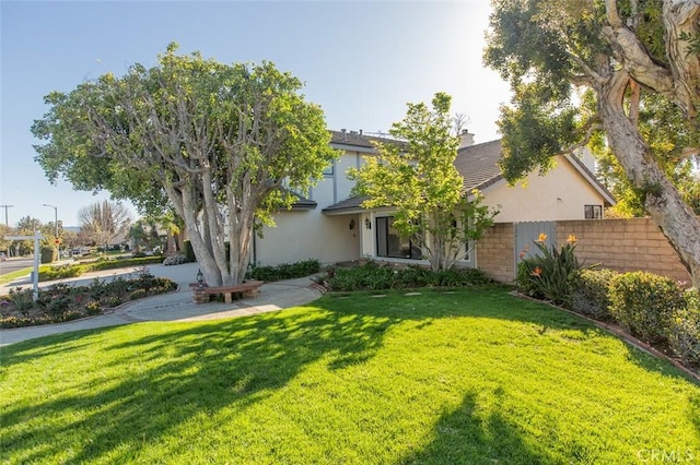 view of property hidden behind natural elements with stucco siding, a front lawn, and fence