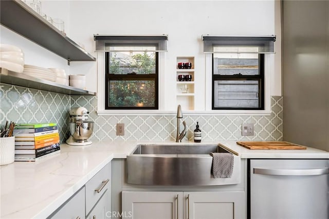 kitchen featuring tasteful backsplash, light stone countertops, dishwasher, and a sink