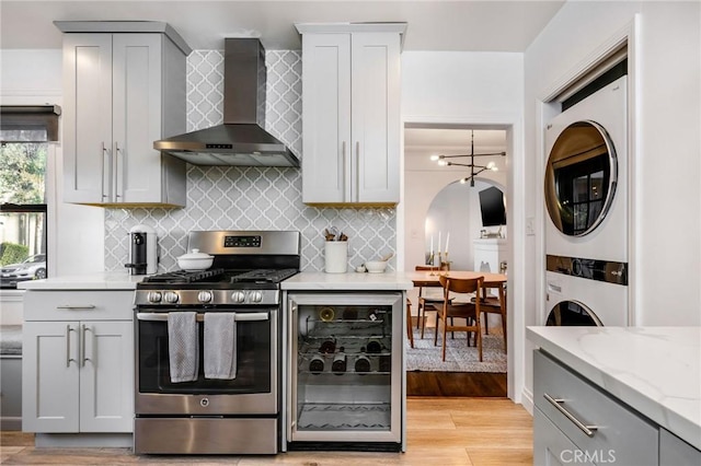 kitchen featuring gray cabinetry, wall chimney range hood, beverage cooler, stacked washer and dryer, and gas stove